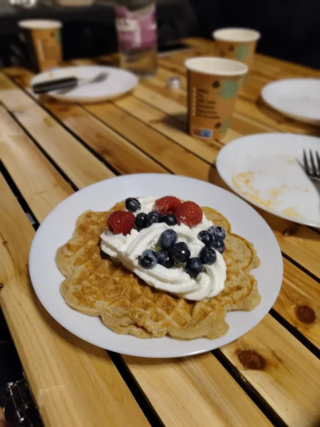 Warme Waffel mit Sahne, Blaubeeren und Himbeeren auf dem Holztisch