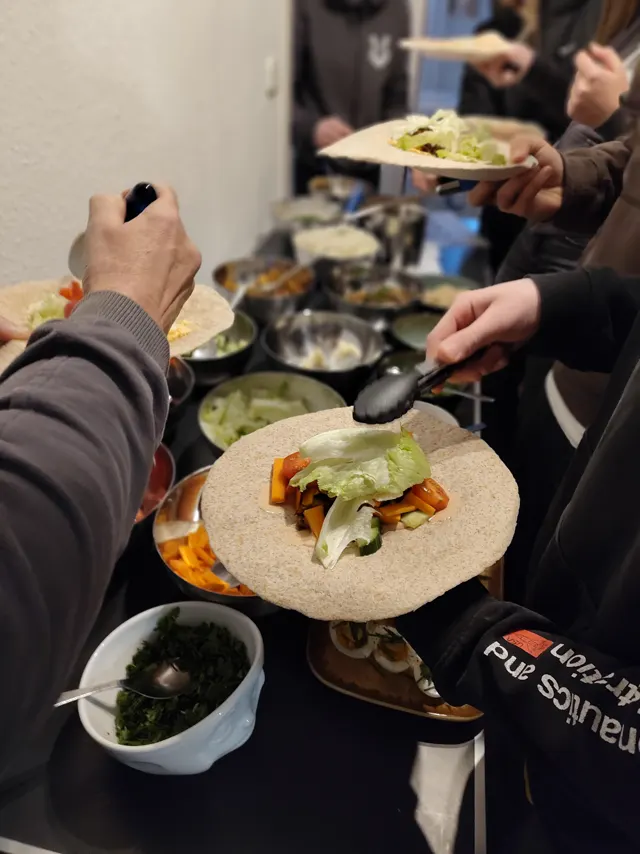 Wraps werden gemeinsam am langen Buffet mit frischem Gemüse befüllt