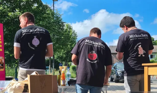 Drei Crew-Mitglieder in Mitkochen-Shirts an der Kochstation im Sommer