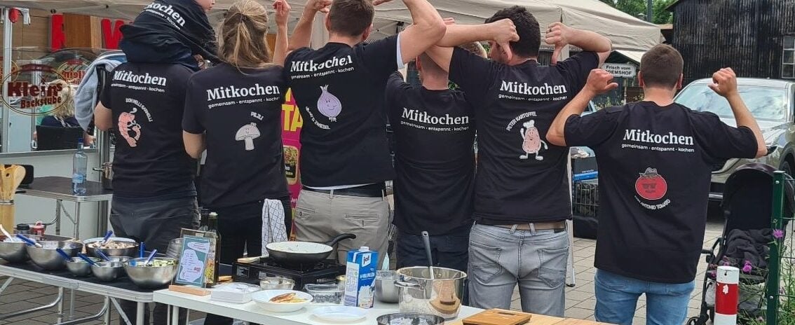 Die Mitkochen-Crew von hinten in schwarzen Shirts – Arme siegreich in die Höhe gestreckt