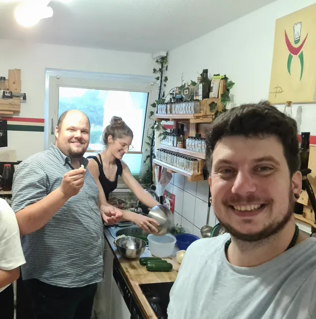 Küchen-Selfie: drei Crew-Mitglieder lachen zwischen Gewürzregal und Spüle